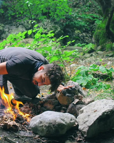 Survivalists: a man crouched in a forest, starting a fire by hand from sticks and stones