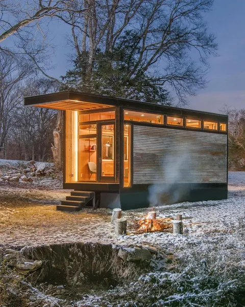 Tiny Homes: a small, warmly-lit tiny home at dusk with a campfire burning outside